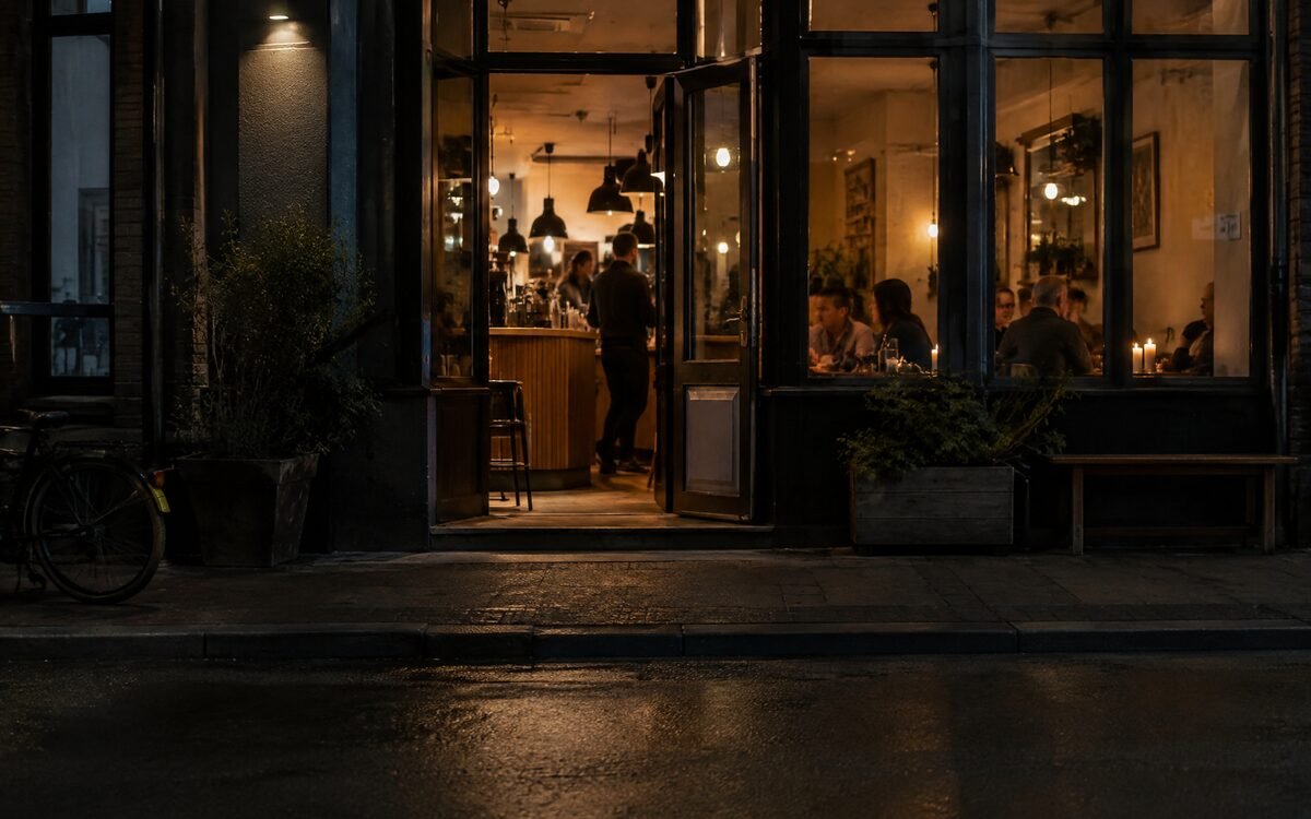 A lit cafe doorway seen from across a quiet street at night — the obvious place to walk into
