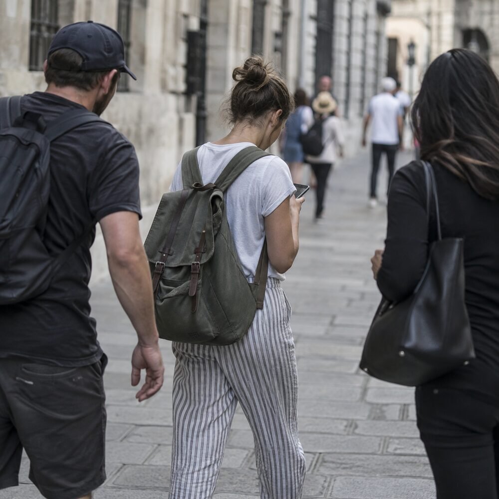 Two people approaching a distracted tourist from opposite sides on a busy pavement