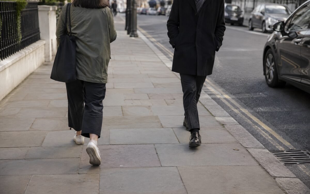 Two people on a pavement with clear space between them, one stepping wide to pass