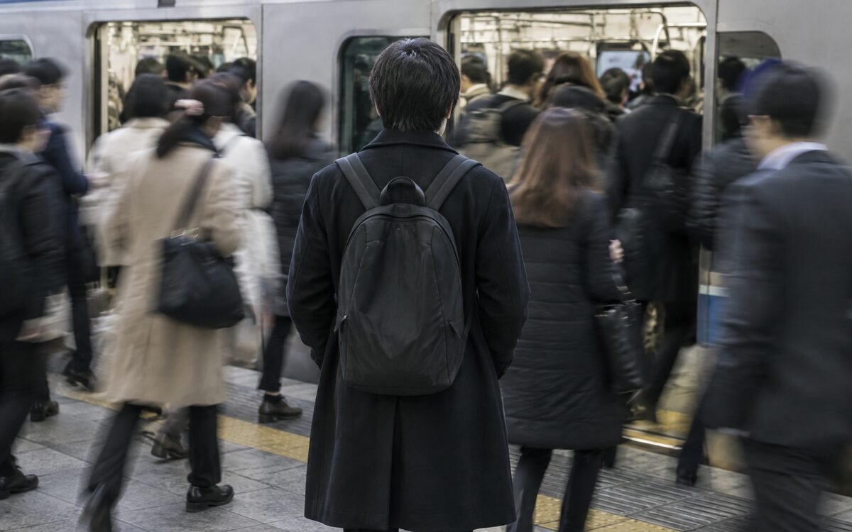 A crowded train platform where one figure stands still while everyone else moves toward the doors