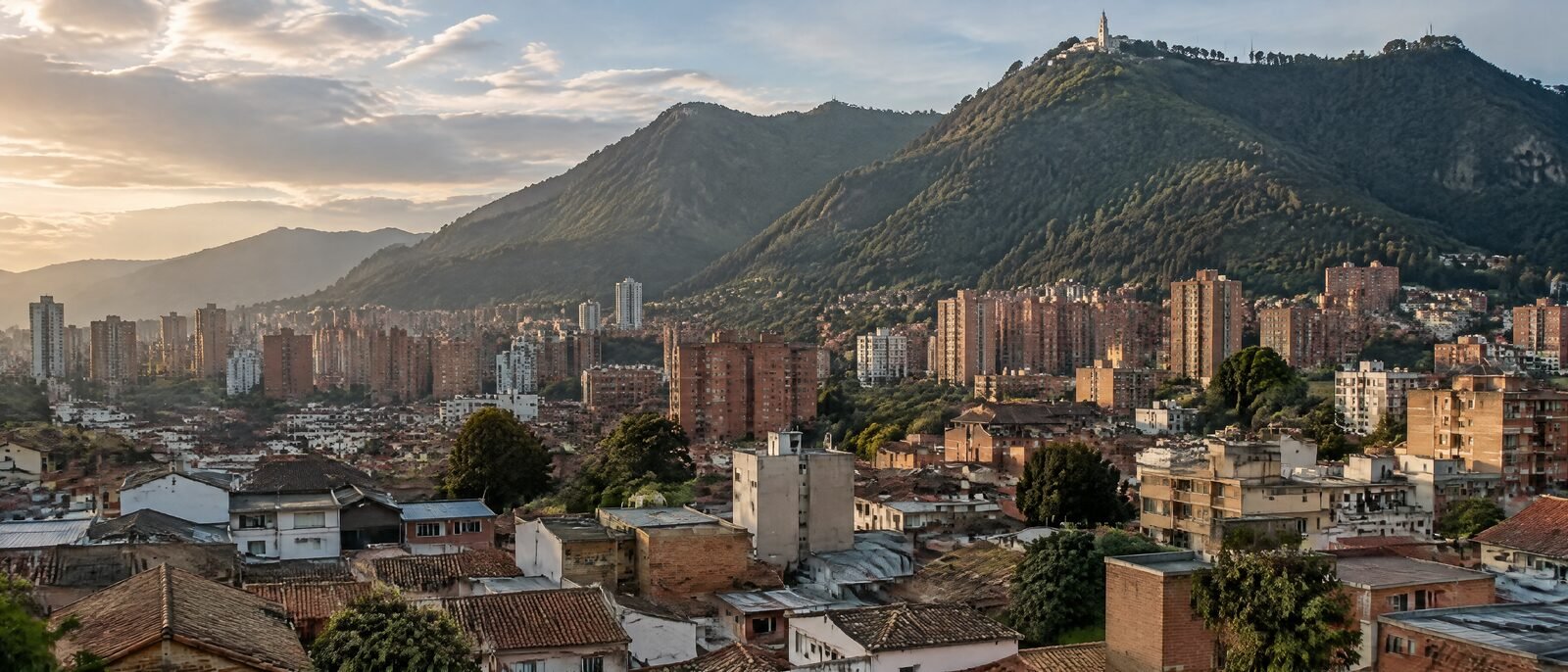 Bogotá rooftops climbing toward the Andean hills below Monserrate in late afternoon light, brick apartment blocks in the foreground