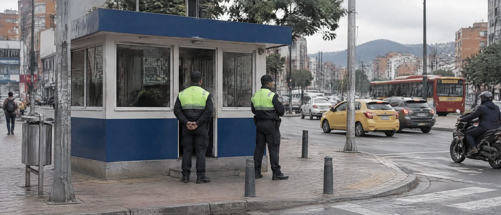 A small blue-and-white CAI police post on a Bogotá street corner in daylight, officers standing outside