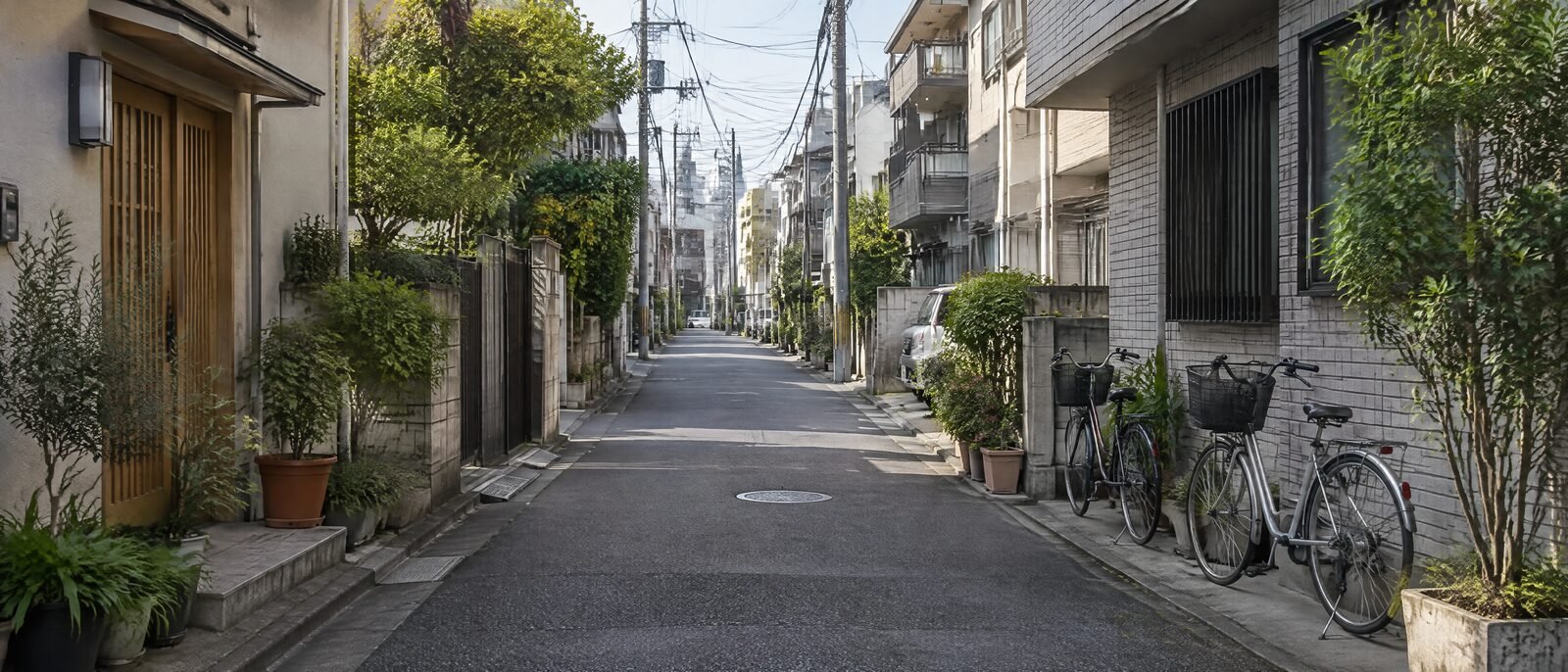 A quiet residential Tokyo street in daylight, low-rise buildings, bicycles parked unlocked against a wall