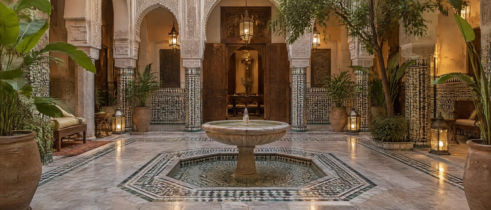 A Marrakech riad courtyard interior, tiled fountain, warm lamplight, empty of people