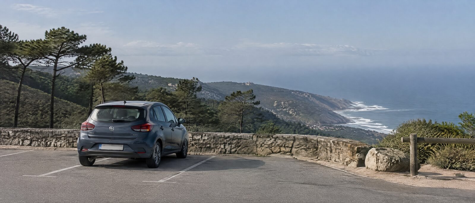 A rental car parked at a coastal viewpoint car park near Sintra, boot visible, nobody around