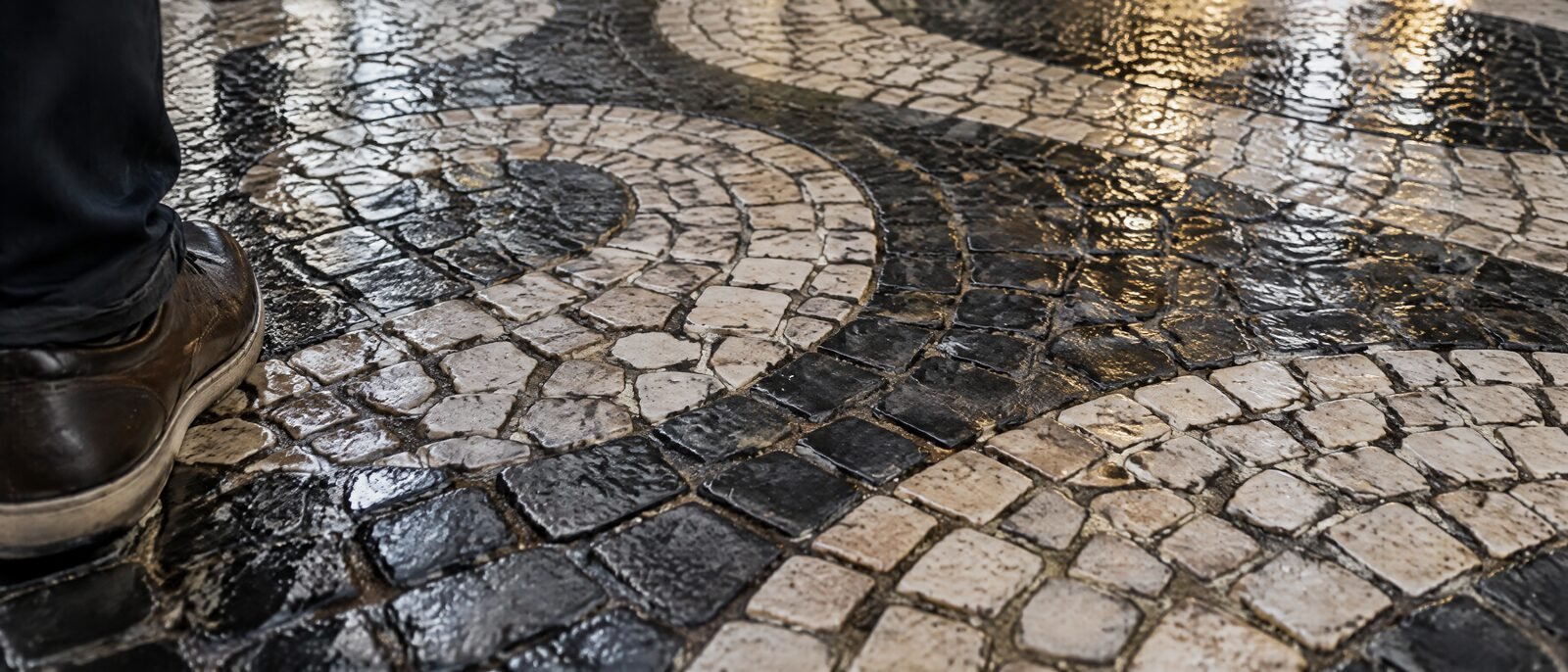 A close view of Lisbon's calcada portuguesa pavement — worn, polished limestone cobbles, wet